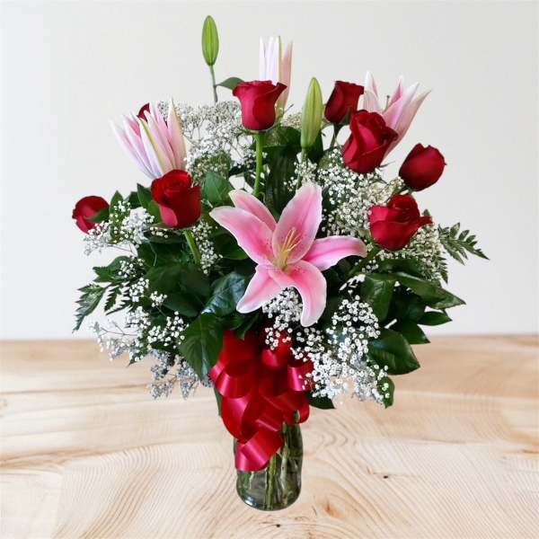 Bouquet of red roses and pink lilies in a glass vase with a red ribbon