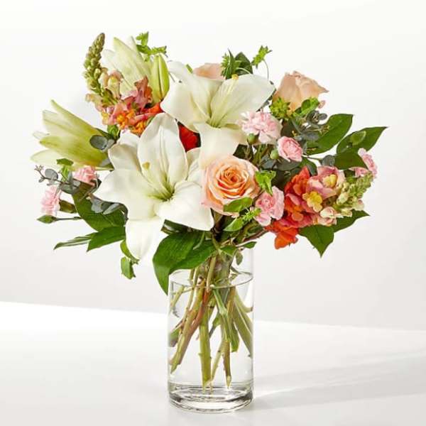 Bouquet of white lilies and peach roses in a clear glass vase