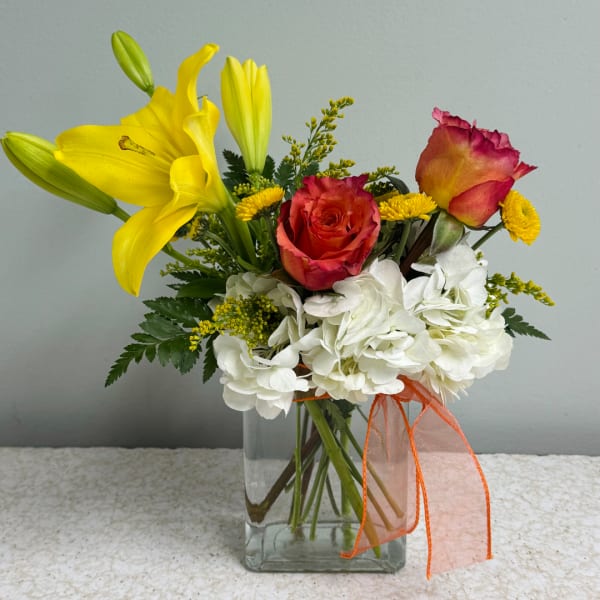 Yellow lilies and red roses in a clear glass vase with white hydrangeas