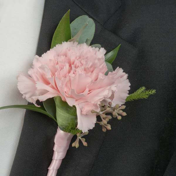 Pink carnation boutonniere with ribbon wrap on a dark suit lapel