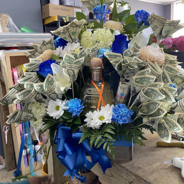 Large bouquet with blue flowers, white blooms, and dollar bills around a tequila bottle