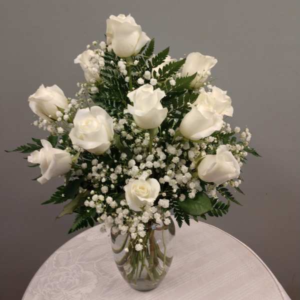 White roses arranged in a clear glass vase with baby's breath