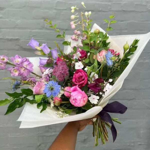 Hand-tied bouquet of pink, purple, and blue flowers wrapped in white paper