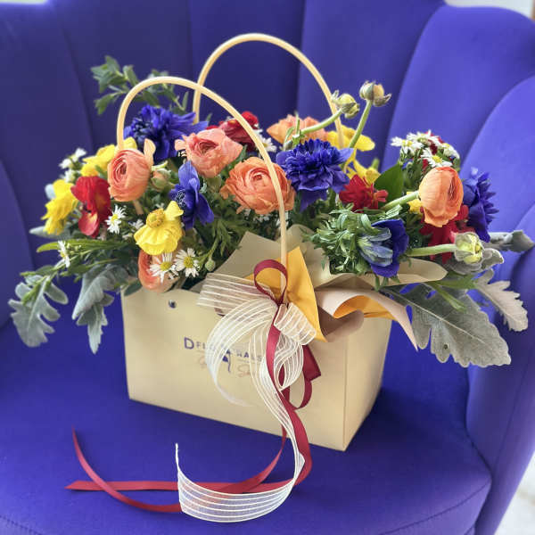 Mixed bouquet in a beige gift bag with peach, yellow, red, and blue flowers