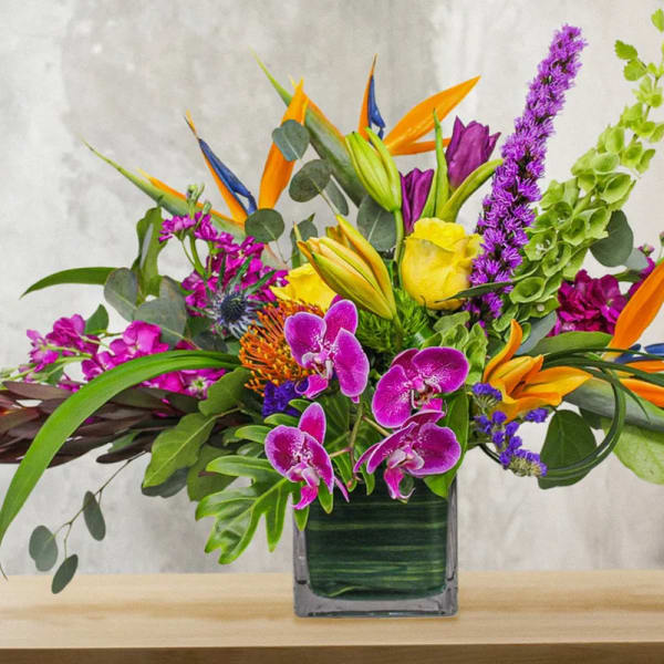 Tropical bouquet with purple orchids and orange bird-of-paradise in a square vase