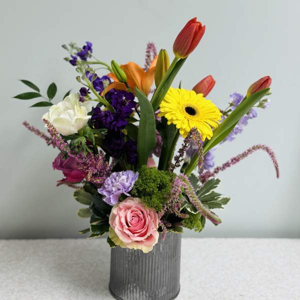 Mixed bouquet in a gray vase with tulips, roses, and a yellow gerbera daisy
