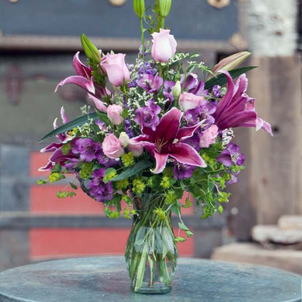 Pink and purple lilies and roses in a clear glass vase
