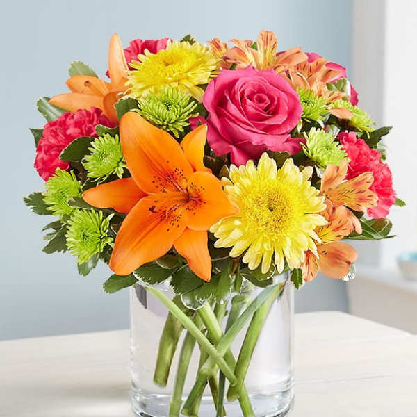 Mixed bouquet of roses, lilies, and chrysanthemums in a clear glass vase