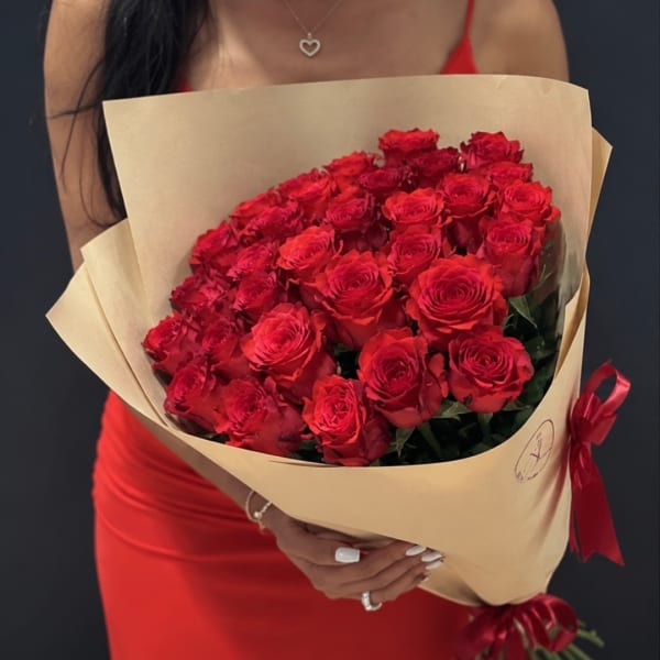 Woman holding a large bouquet of red roses wrapped in tan paper