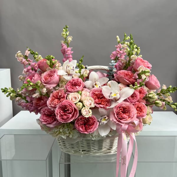 Pink rose and orchid arrangement in a white wicker basket with a ribbon