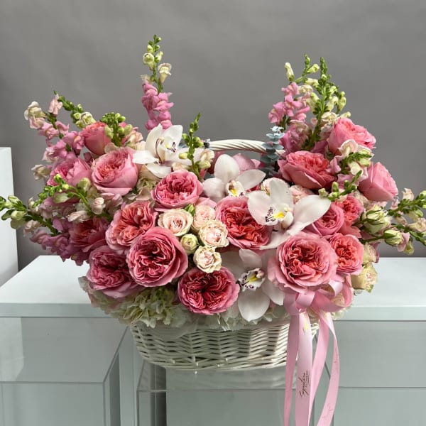 Pink roses and white orchids arranged in a white basket with a ribbon