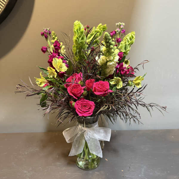 Bright pink roses and yellow flowers in a clear glass vase with a white bow