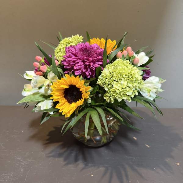 Mixed bouquet with sunflowers, purple mums, and pale green hydrangeas in a glass vase