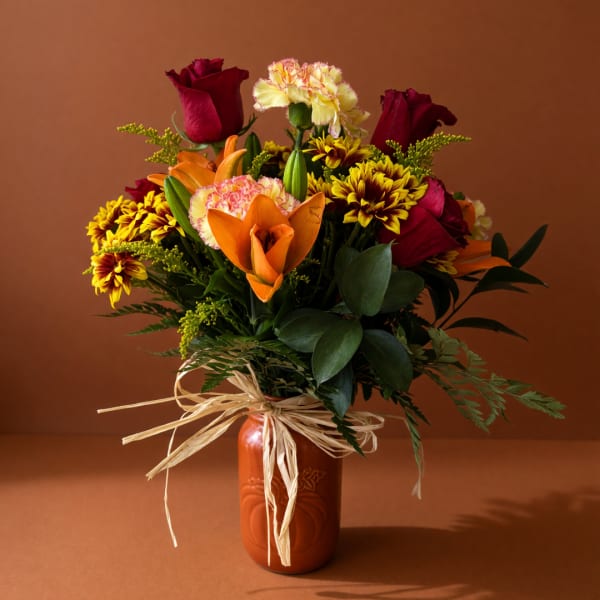 Bouquet of red roses, orange lilies, and yellow chrysanthemums in an orange vase