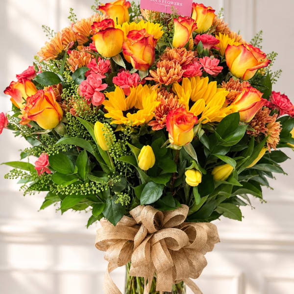 Bouquet of yellow-orange roses, sunflowers, and pink chrysanthemums tied with burlap ribbon