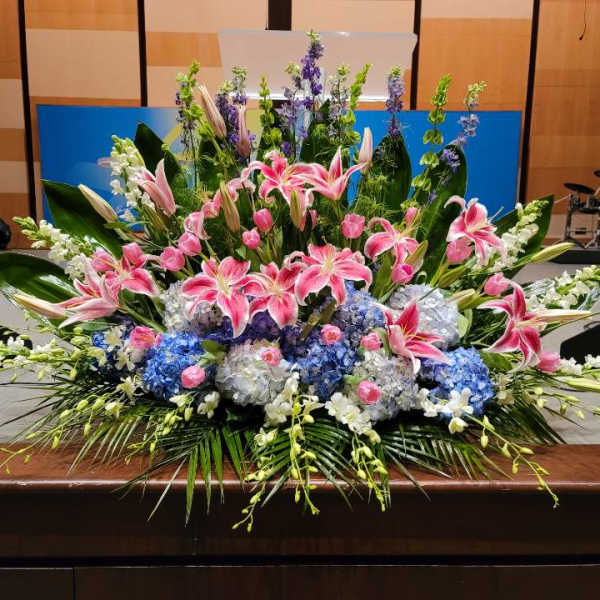 Large altar-style arrangement of pink lilies, blue hydrangeas, and white flowers in a fan shape