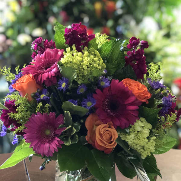 Mixed bouquet of magenta, orange, and purple flowers in a glass vase