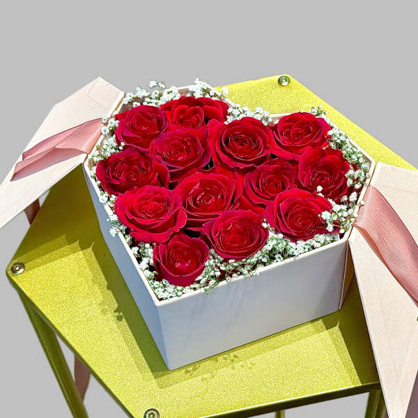 Box of red roses with pink ribbons on a gold stand