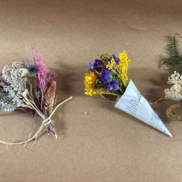 Three small dried flower bouquets on brown paper, including purple, yellow, and white arrangements