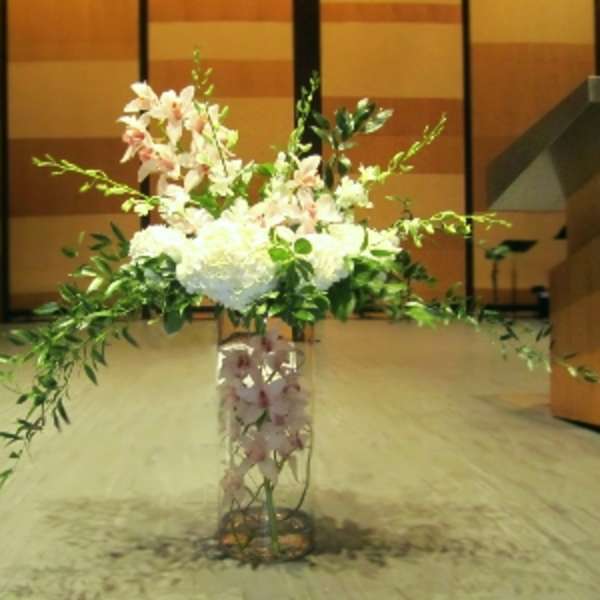 Tall arrangement of white hydrangeas and pink orchids with trailing greenery in a clear glass vase
