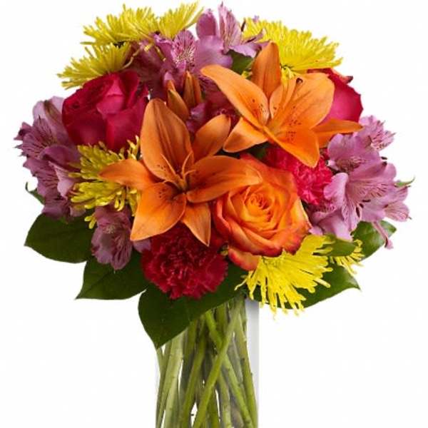 Colorful bouquet of lilies, roses, and daisies in a clear glass vase