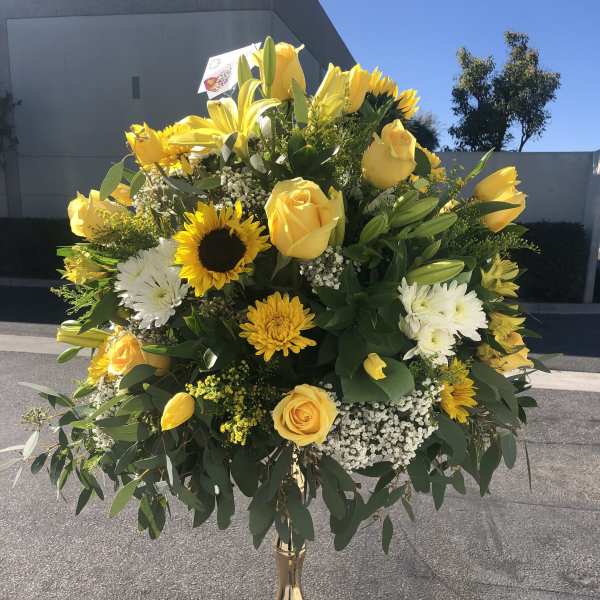 Yellow roses and mixed blooms arranged in a tall gold vase
