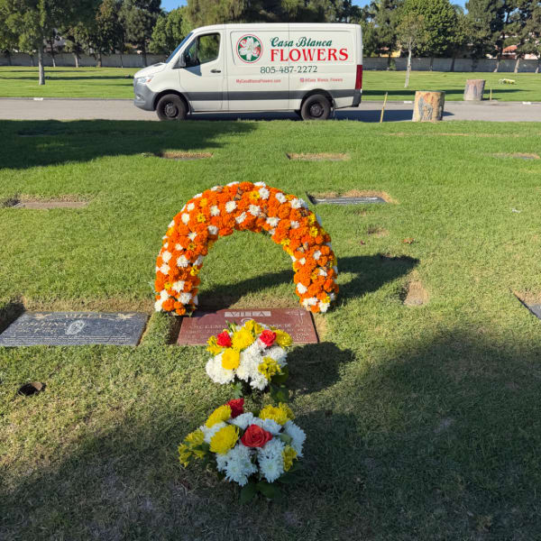 Orange and white floral wreath with two small bouquets on a gravesite