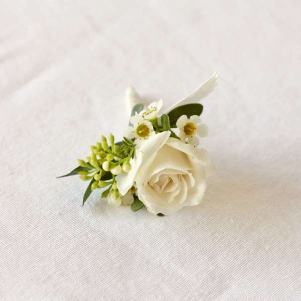 White rose boutonniere with small white blossoms and greenery