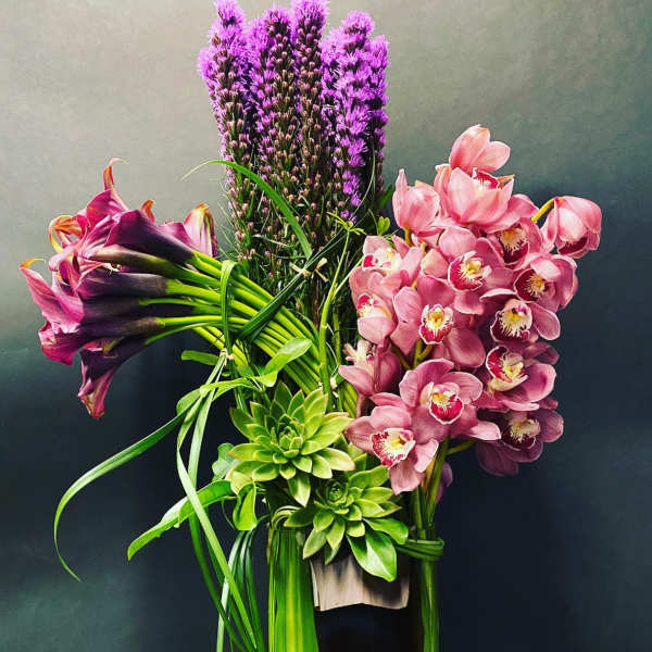 Tall arrangement of pink orchids, purple flowers, and green succulents in a vase
