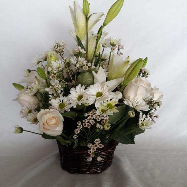 White lilies and roses arranged in a dark woven basket
