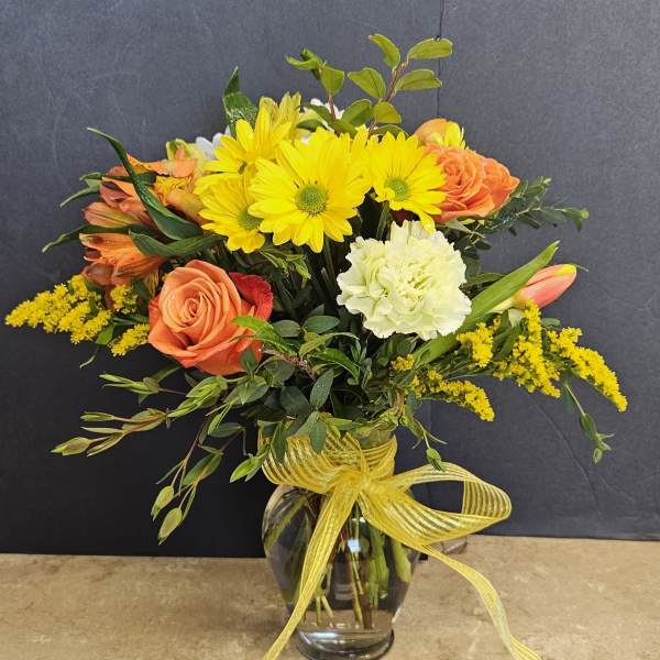 Bouquet of yellow daisies, orange roses, and white carnations in a glass vase