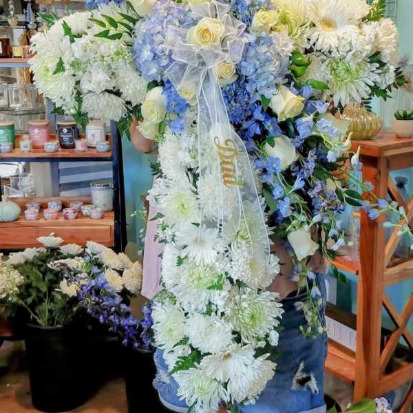 Tall white and blue floral cross spray with yellow roses and a ribbon reading Dad