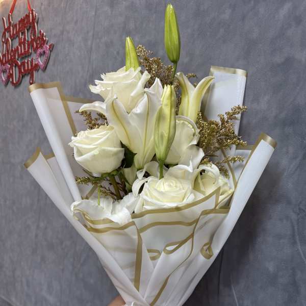 White roses and lilies in wrapped bouquet with gold ribbon