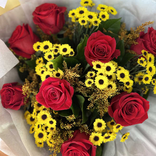 Bouquet of red roses and small yellow daisies wrapped in pale paper