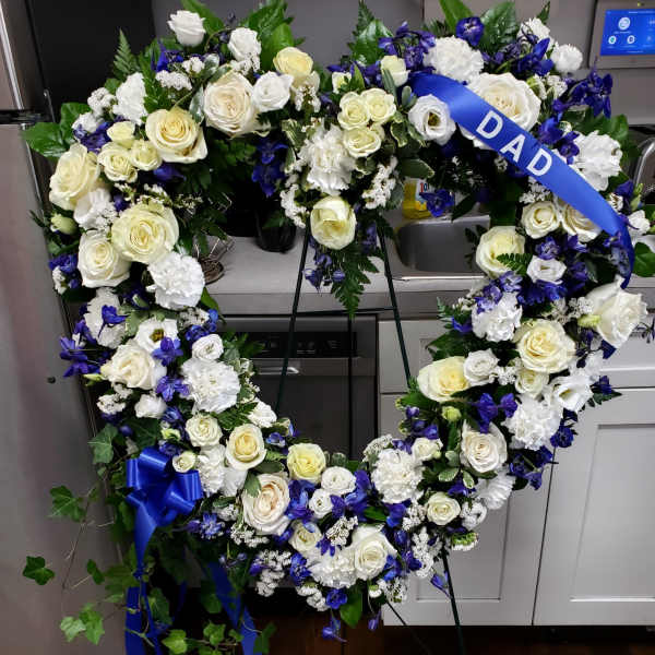 Heart-shaped floral wreath with white roses and blue flowers on a stand