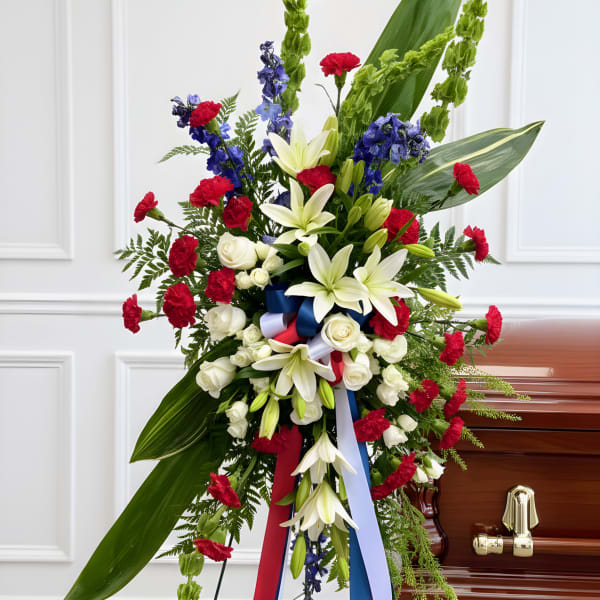 Standing funeral spray with white lilies, red carnations, and blue flowers