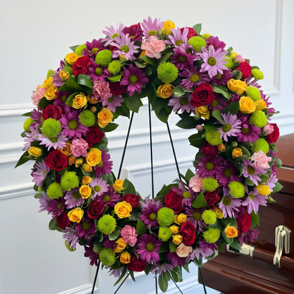 Large floral wreath with roses and daisies on a stand beside a casket