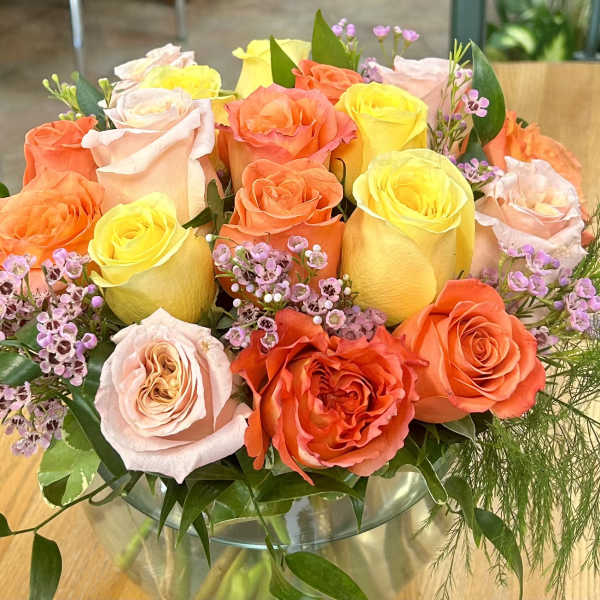Bouquet of orange, yellow, and blush roses in a glass vase