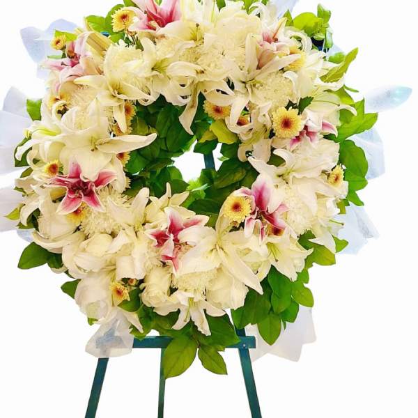 White floral wreath with pink accents on a stand