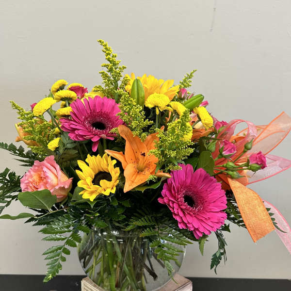 Bright mixed bouquet in a glass vase with pink gerberas, sunflowers, and lilies