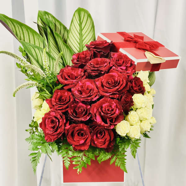 Red and white roses arranged in a gift box with a red ribbon and bow