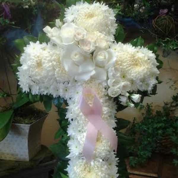 White floral cross arrangement with a pink ribbon