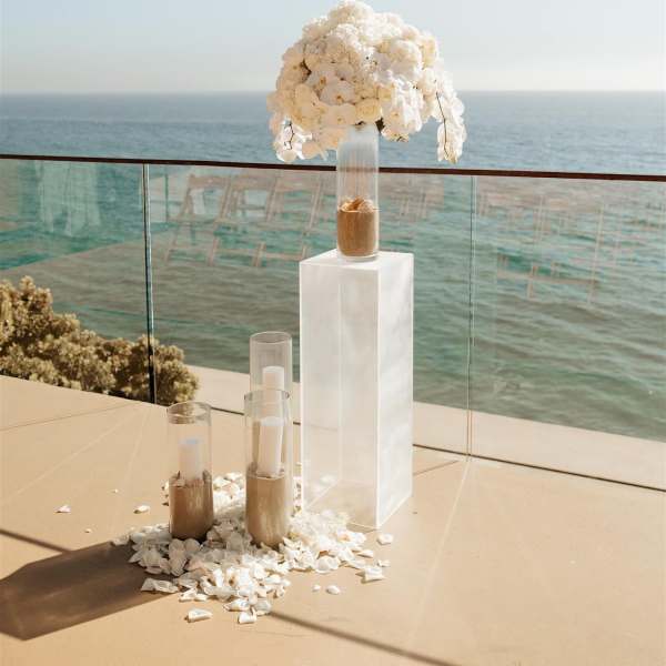 White orchid arrangement on a tall clear pedestal by the ocean