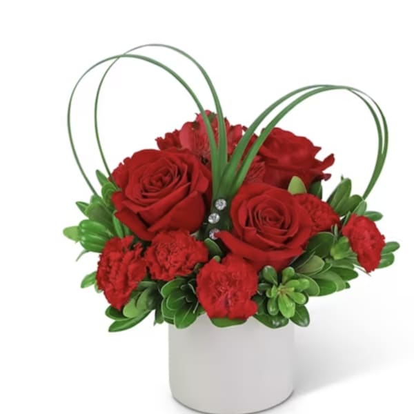 Red roses and carnations in a white vase with green loops
