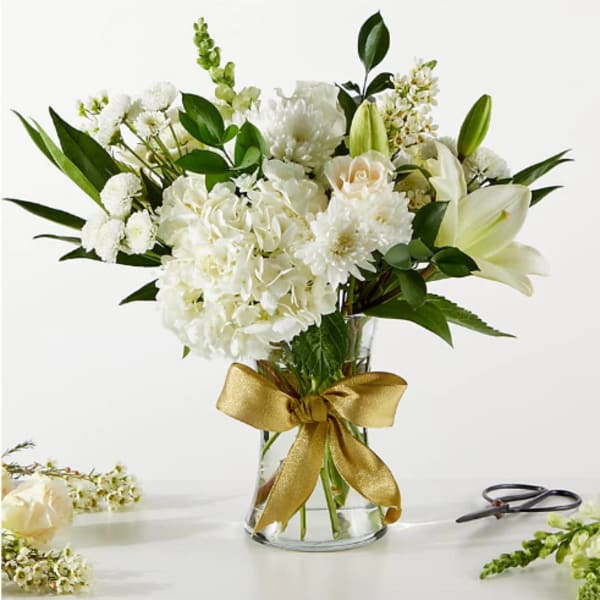 White floral bouquet in a glass vase with a gold ribbon