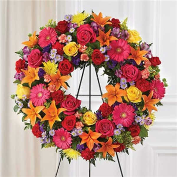 Colorful floral wreath on a stand with roses, lilies, and daisies
