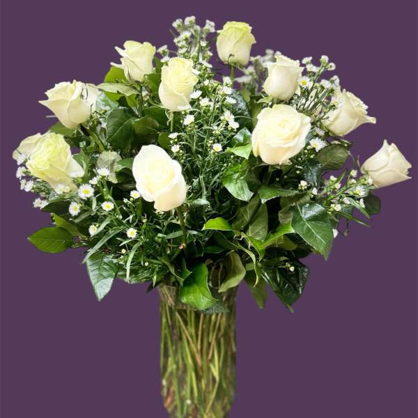 White roses in a clear glass vase with small white filler flowers
