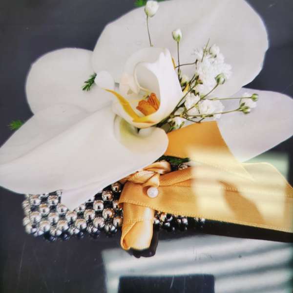 White orchid wrist corsage with small white blooms, gold ribbon, and rhinestone bracelet.
