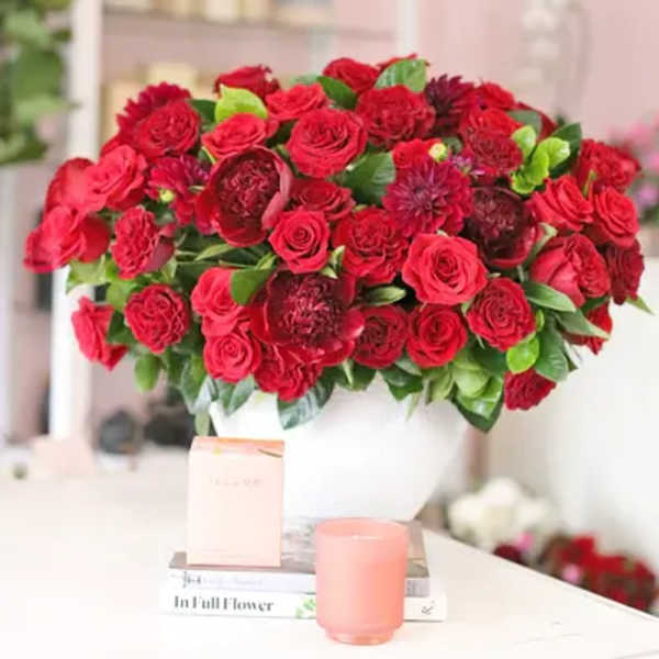 Red rose arrangement in a white vase with green leaves