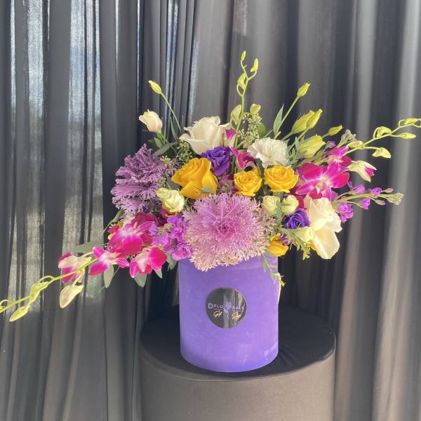 Colorful bouquet in a purple hatbox with yellow, pink, white, and purple flowers